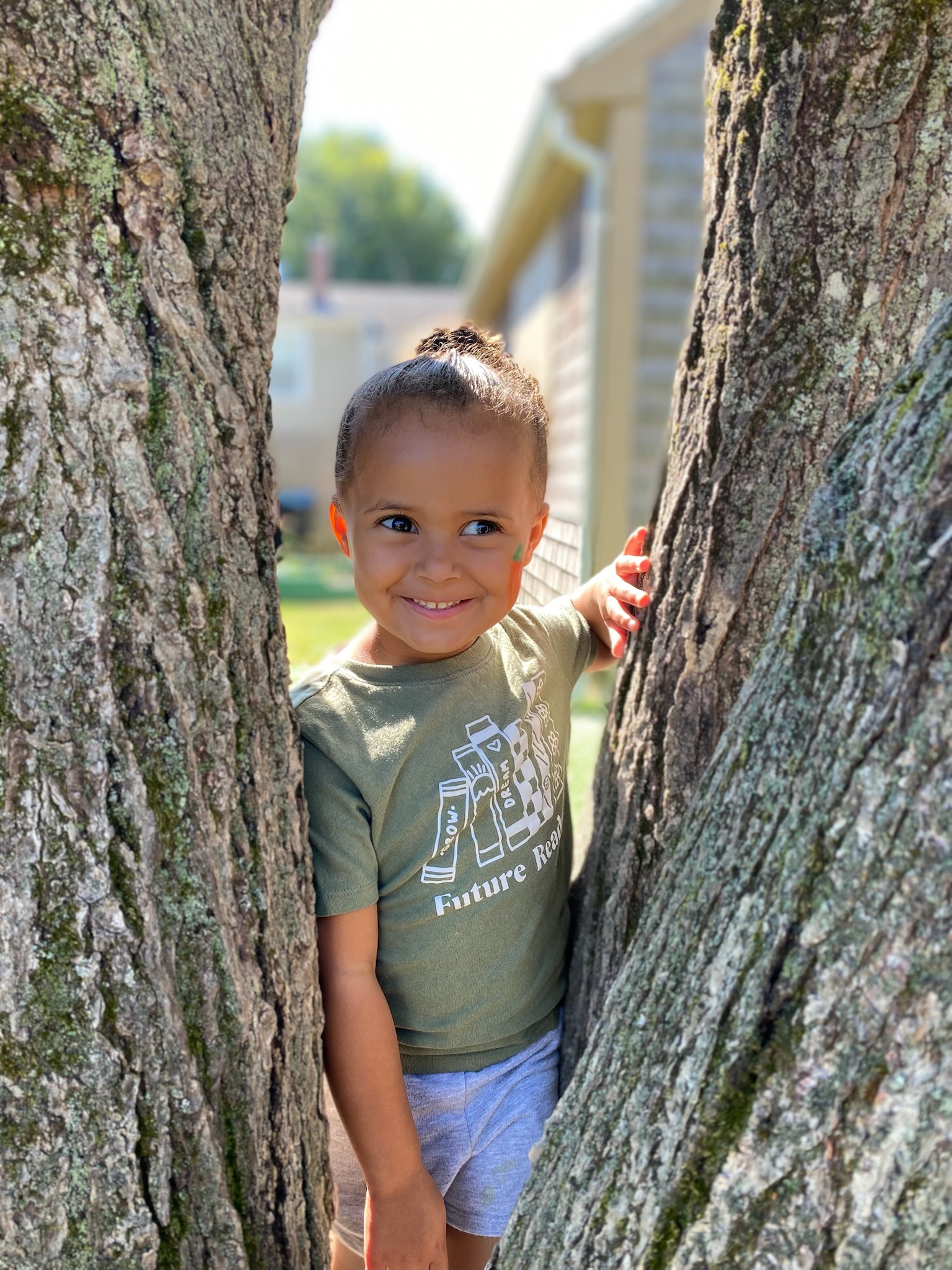 Child peeking between two tree trunks outdoors