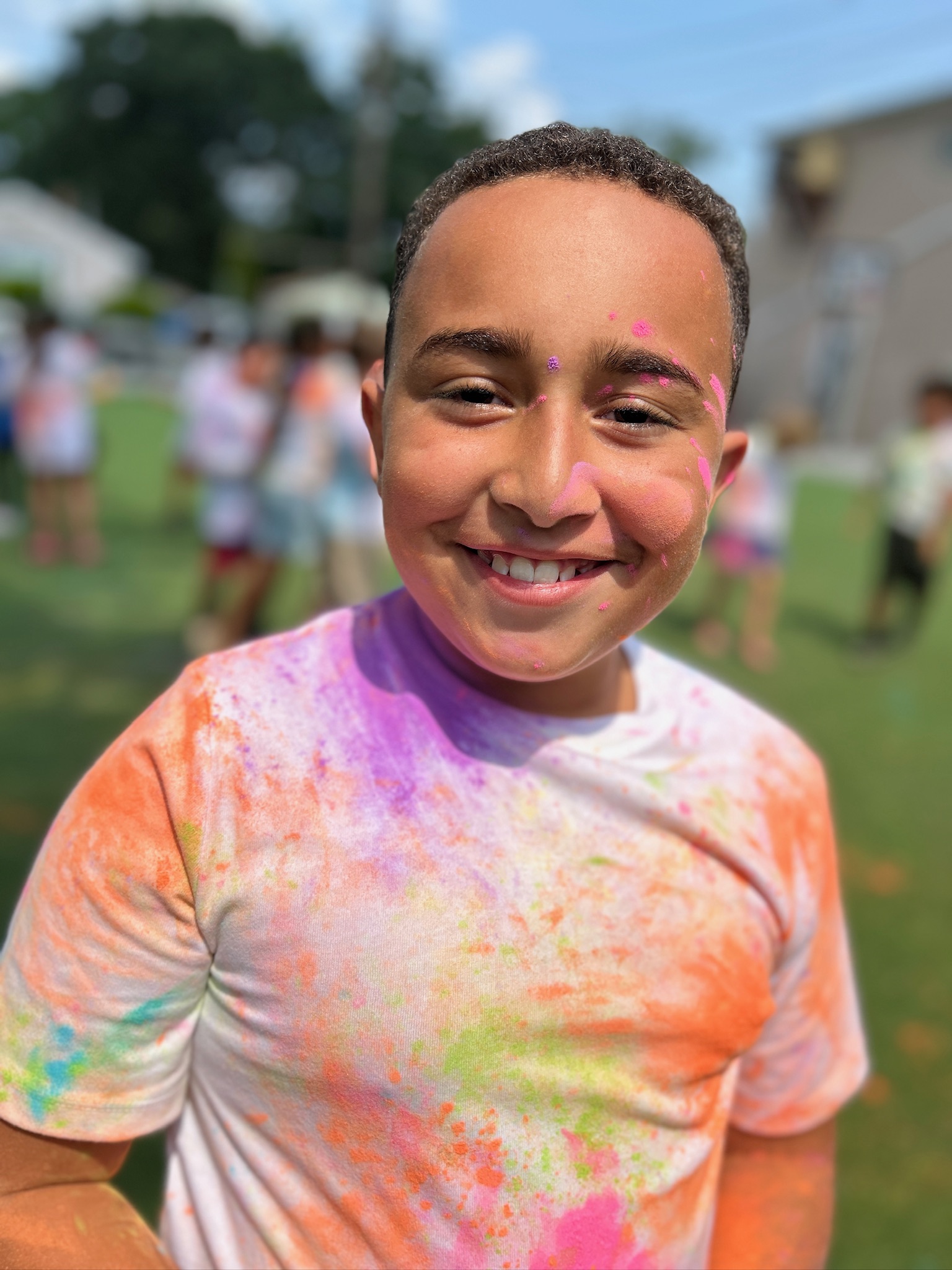 Boy smiling covered in colorful powder at outdoor event