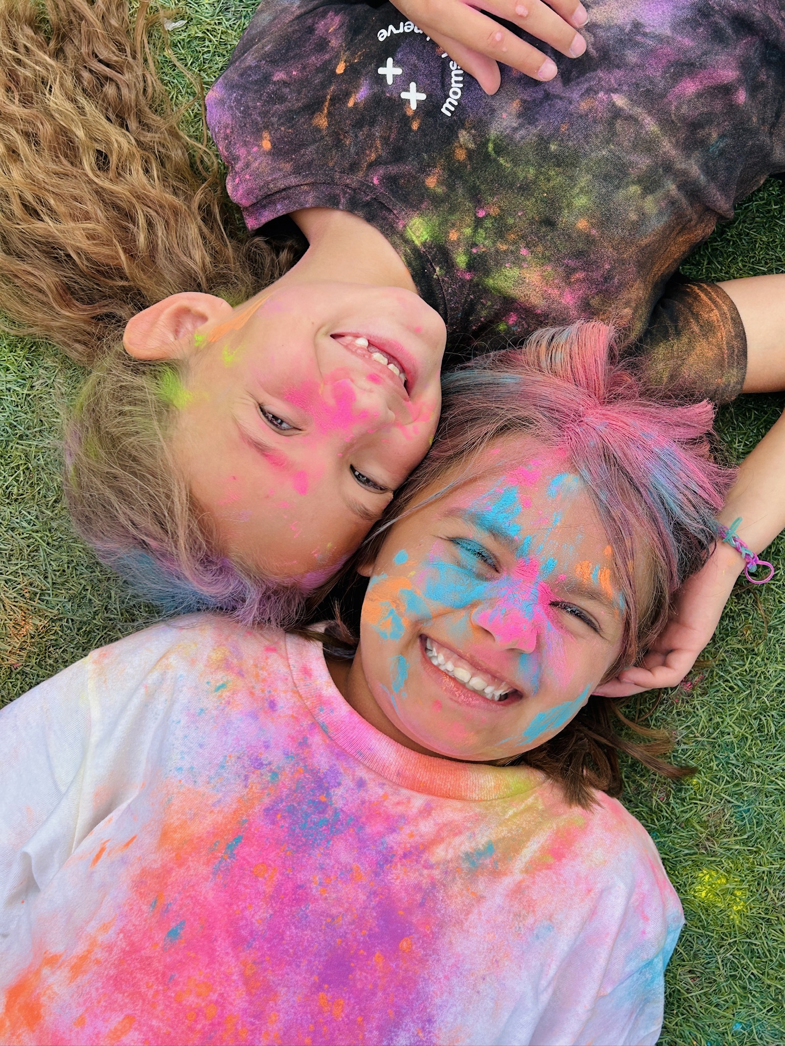 Two friends lying on the grass covered in color run paint