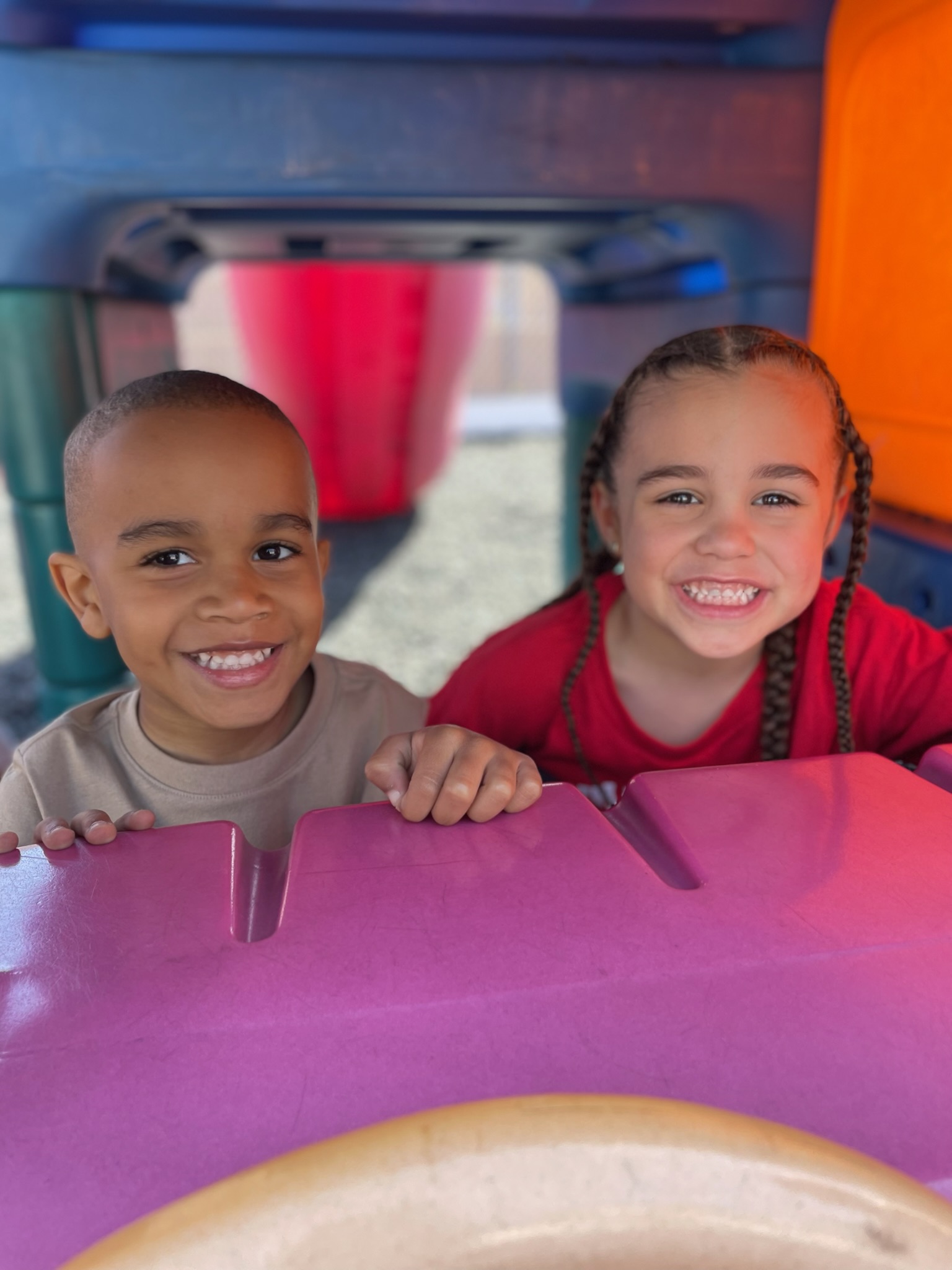 Two children smiling on colorful playground